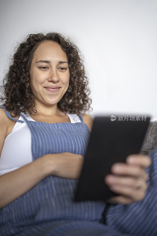 Happy pregnant woman reading on electronic tablet